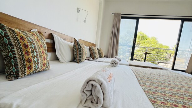 A hotel room with a large bed, multiple pillows, a white blanket, and a view of greenery outside. - Hotel Ambatoloaka (Nosy Be)