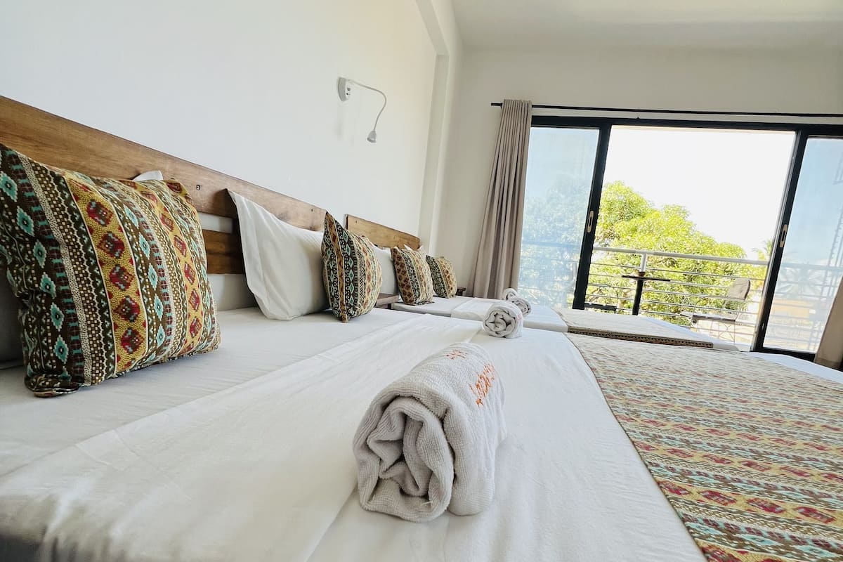 Habitación de hotel con una cama grande, varias almohadas, una manta blanca y vistas a zonas verdes.