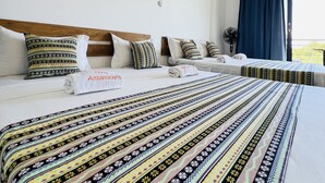 A hotel room with two beds, a wooden headboard, patterned bedspreads, and a view of the outdoors. - Hotel Ambatoloaka (Nosy Be)