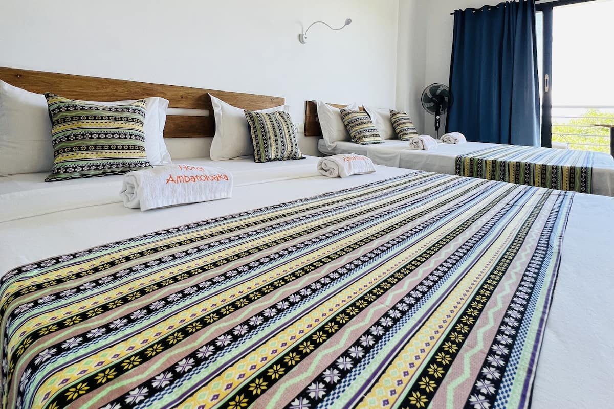 Habitación de hotel con dos camas, cabecera de madera, colchas estampadas y vistas al exterior.