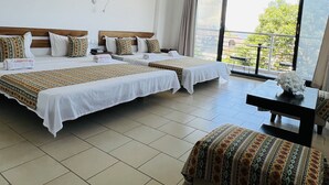 A hotel room with two beds, a small table, and a view of the outdoors. - Hotel Ambatoloaka (Nosy Be)