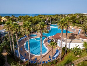 A resort with multiple swimming pools surrounded by palm trees, lounge chairs, and a view of the ocean. - Sagitario Princesa Playa (Ciutadella de Menorca)