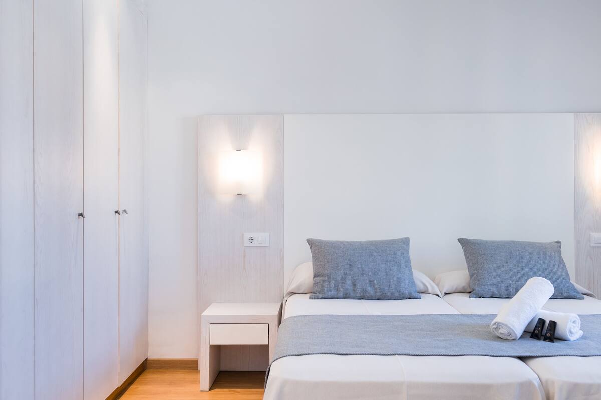 A bedroom with a bed, two pillows, a bedside table, and a nightstand.