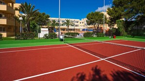 A tennis court with a net, surrounded by greenery and buildings in the background. - Sagitario Princesa Playa (Ciutadella de Menorca)