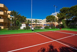 A tennis court with a net, surrounded by greenery and buildings in the background. - Sagitario Princesa Playa (Ciutadella de Menorca)