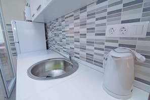 Een moderne keuken met een roestvrijstalen spoelbak, een waterkoker en een betegelde spatwand.