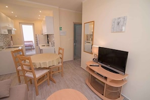 Een compact woongedeelte met een eethoek, kitchenette en een televisie op een houten standaard.