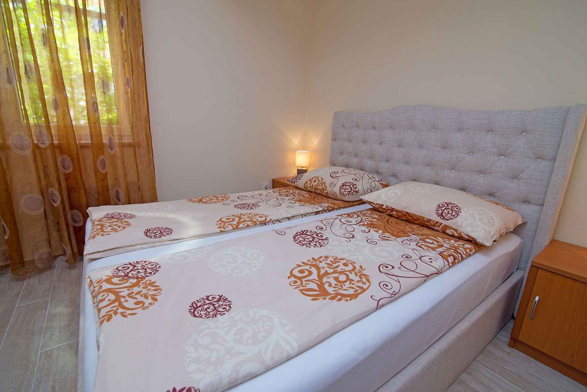 Una cama doble con cabecera capitonada, una mesita de noche con lámpara y un mueble auxiliar de madera.