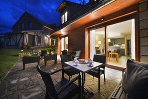 Een modern huis met een patio, buitenzitplaatsen en een grote schuifpui naar een binnenshuis gelegen keuken.