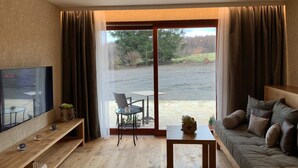 Una sala de estar moderna con un televisor de pantalla plana, una mesa de centro de madera, un sofá y un gran ventanal corredizo que da a un espacio al aire libre.