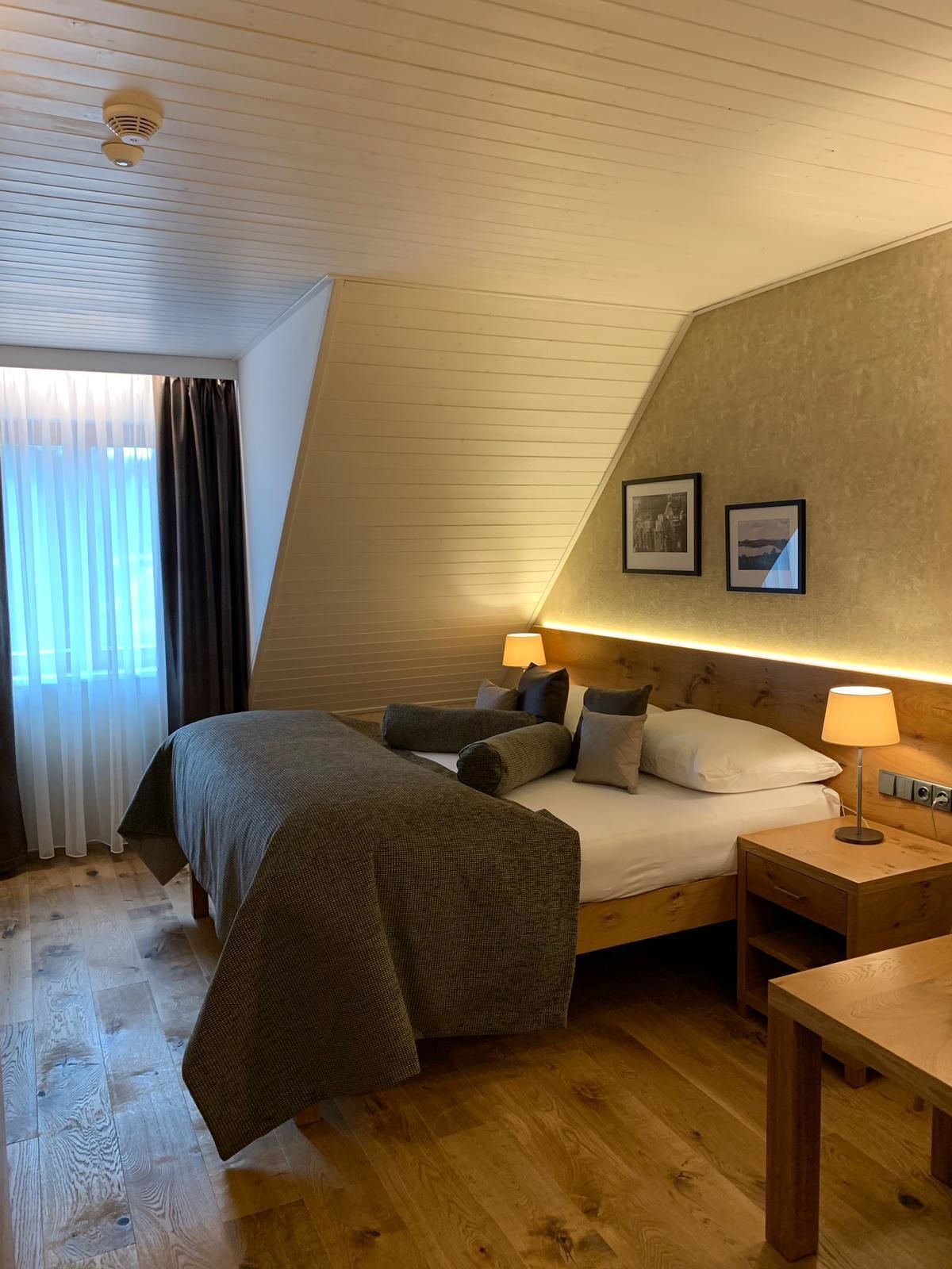 Ein gemütliches Schlafzimmer mit Bett, Nachttisch, Lampe und einem Fenster mit Vorhängen.