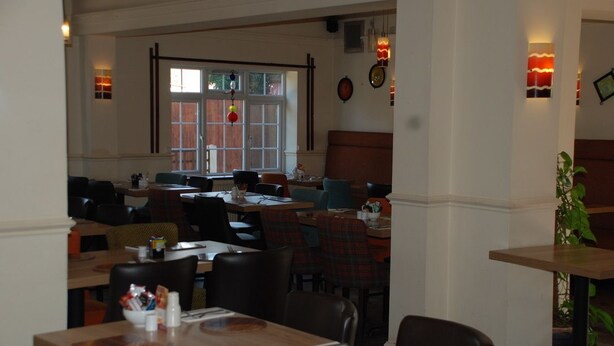 En restaurant med flere borde og stole, et stort vindue med udsigt og vægmonterede lamper.