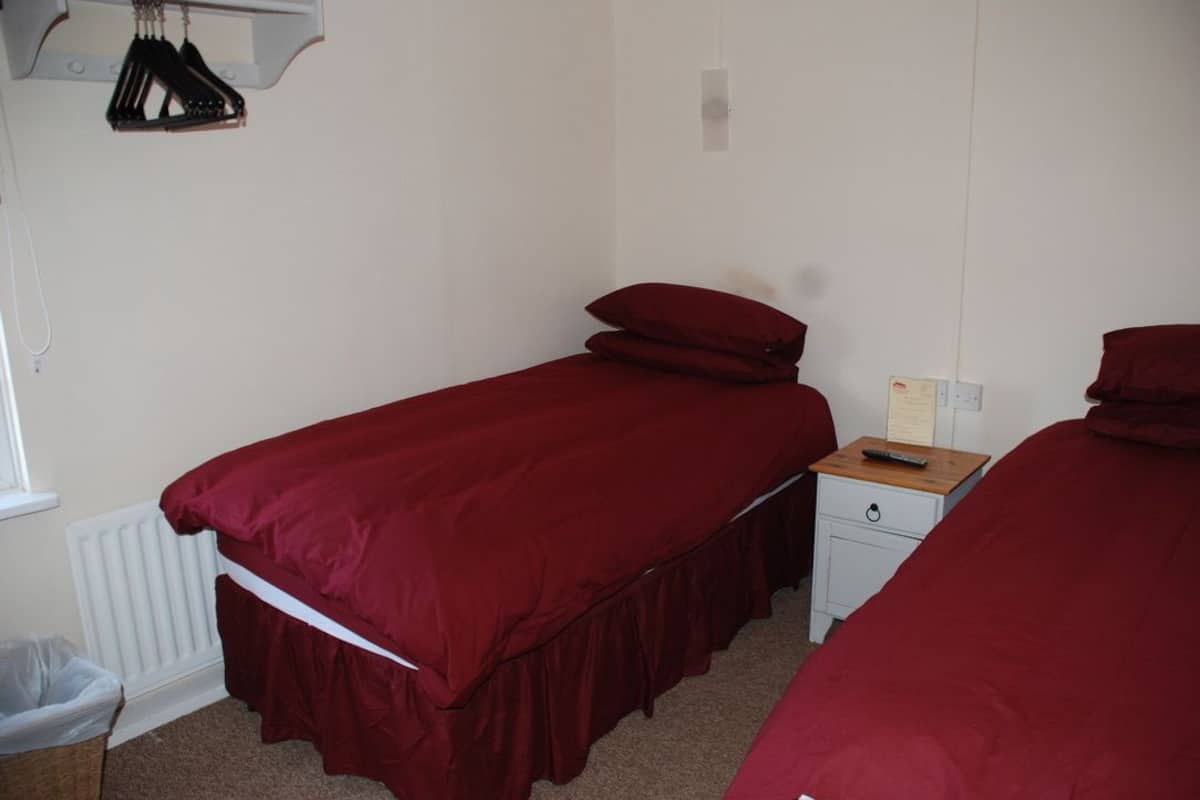 A bedroom with two single beds, a small bedside table with a lamp, and a radiator.