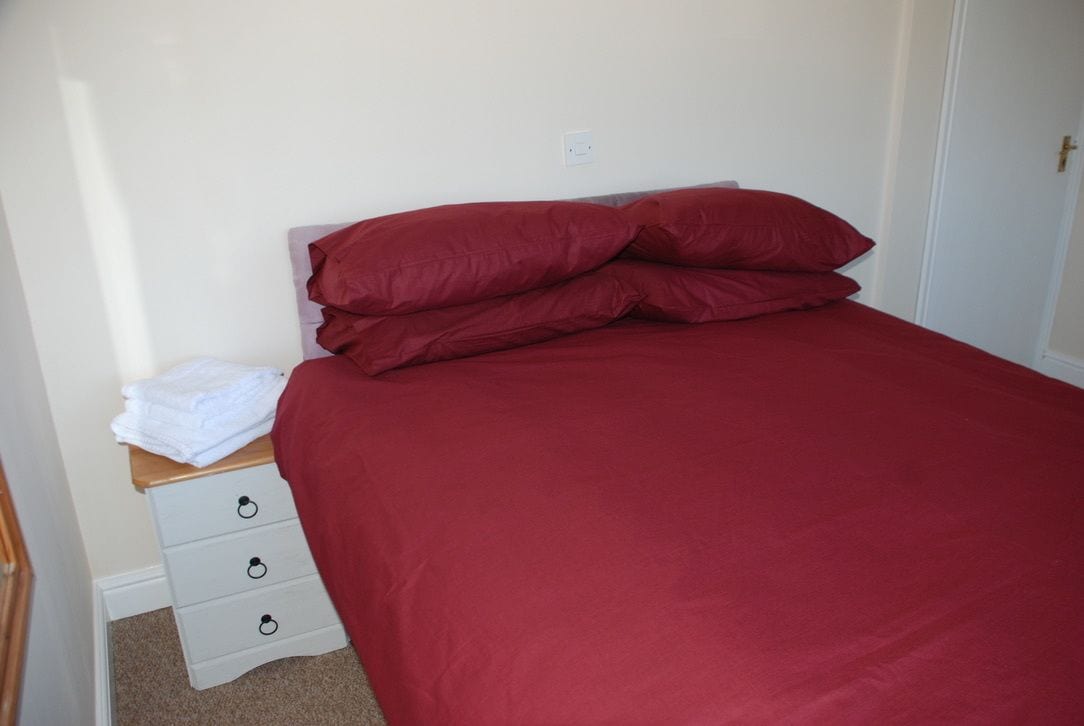A bedroom with a bed, a nightstand, and a drawer unit.