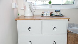 Et hvidt kommode med sorte ringgreb, en hvid elkedel, en bakke med teposer og en lille plante på et vindueskar.