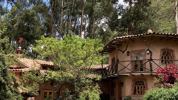A traditional building with a stone pathway leading to the entrance, surrounded by lush greenery and flowering plants.