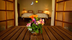 A wooden table with a floral arrangement in the foreground, a bed with a moon projection on the wall, and a night sky visible through a window.