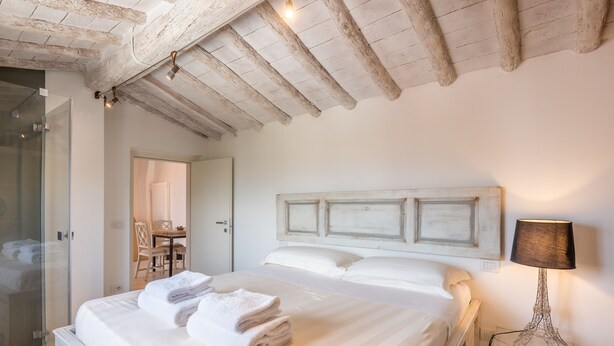 Een slaapkamer met een groot bed, een houten plafond, een bedlampje en een douchecabine van glas.