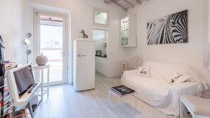 Een moderne woonkamer met een witte bank, een flatscreen-televisie, een kleine tafel en een boekenplank.