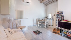 Een moderne woonkamer met een bank, een eettafel en een televisie. Er is een boekenplank vol boeken en een bijzettafeltje met een boek erop.