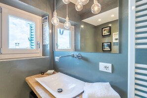 Une salle de bain avec un lavabo blanc, une serviette, un miroir et une fenêtre donnant sur le ciel.