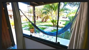 A hammock tied between window bars, overlooking a garden with potted plants and a palm tree. - Da Ferradura (Búzios)