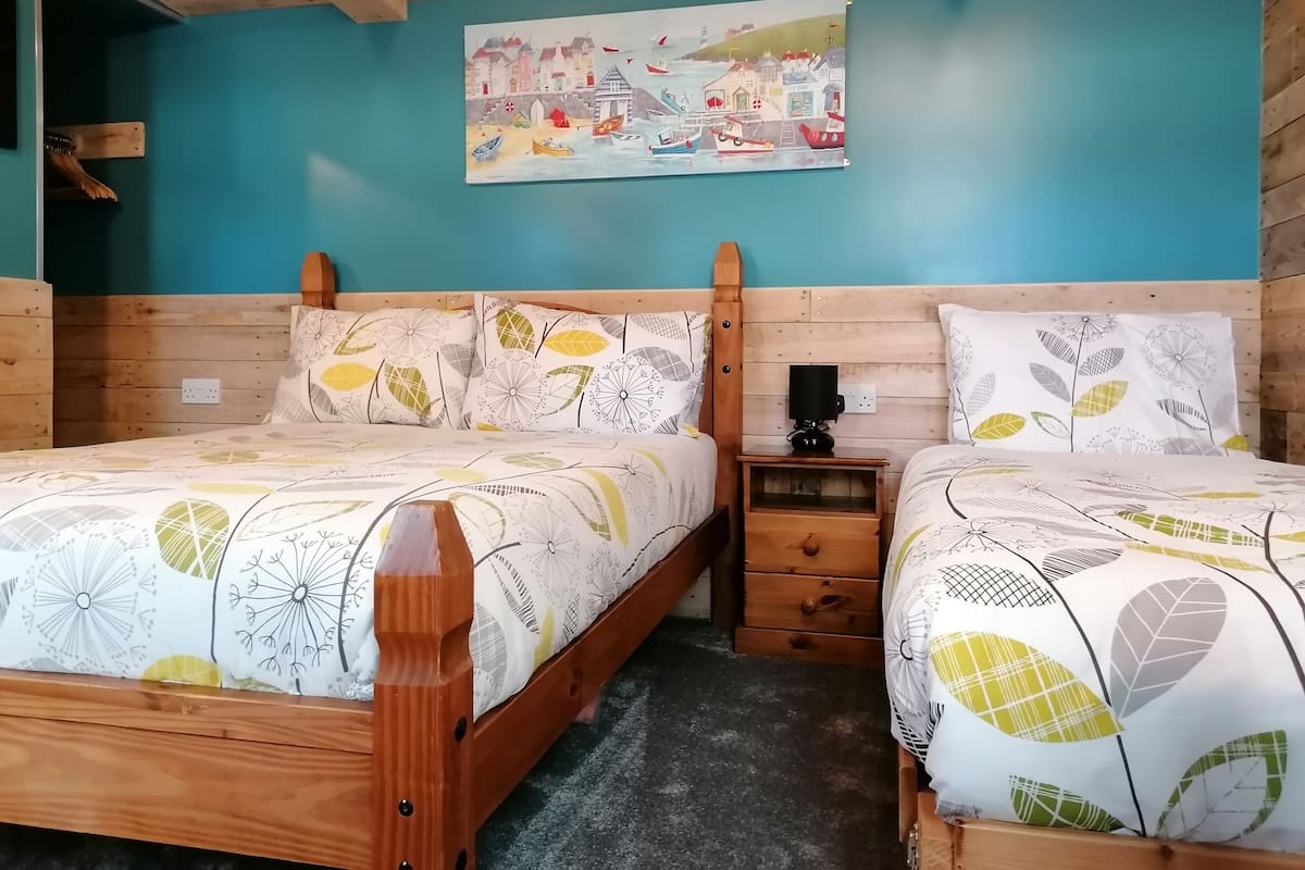 Une chambre confortable avec deux lits en bois, une table de chevet et un tableau représentant un paysage côtier.