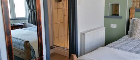 Quarto com cama de madeira, um espelho grande, radiador, um quadro e porta que dá para outro cômodo.