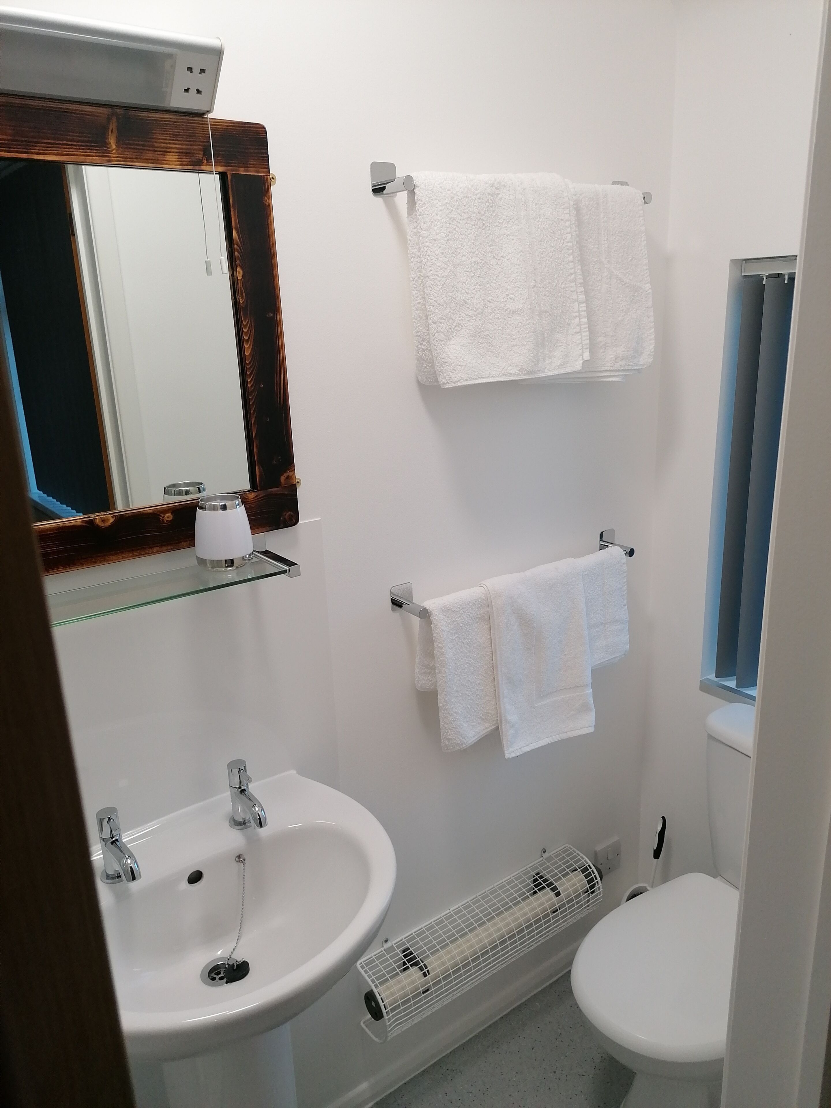 Une salle de bain avec deux lavabos, des toilettes, un miroir avec un cadre en bois et deux serviettes suspendues à des crochets.