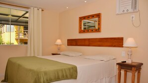 Habitación de hotel con cama, dos lámparas de noche, cabecera de madera, espejo y ventana con cortinas.