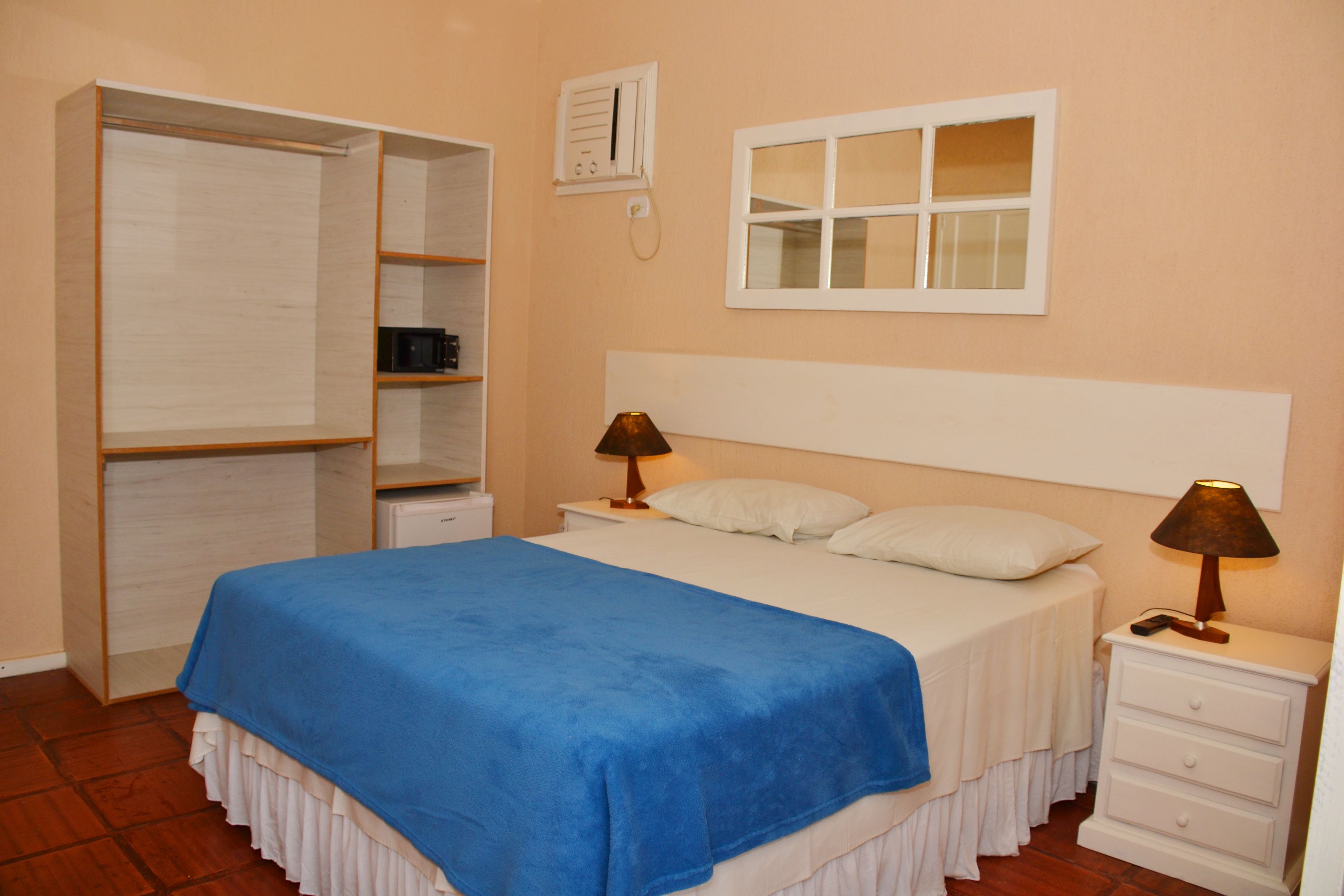 A bedroom with a bed, two bedside tables, a nightstand, a wardrobe, and a window.