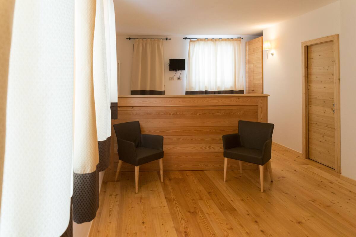 A room with two chairs, wooden flooring, a wooden reception desk, a flat-screen TV, and a wooden door.