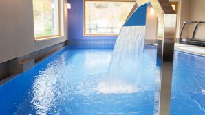 Una piscina interior amb cascada, grans finestres i una cinta de córrer.
