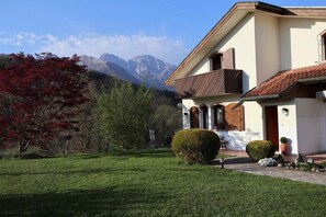 Una casa con césped cuidado, un balcón de madera y montañas al fondo.