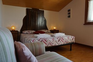 Un dormitorio con cabecera de madera, cama con ropa de cama estampada, dos lámparas de noche y una ventana con cortinas.