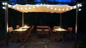 An outdoor patio with a pergola covered by a white canopy, string lights, and wooden tables and chairs. - Bed & Breakfast La Pecora Nera (Belluno)