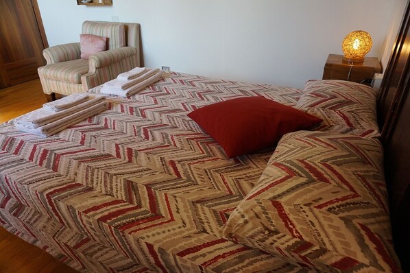 A bed with patterned bedding and a red pillow, a chair, and a bedside lamp. - Bed & Breakfast La Pecora Nera (Belluno)