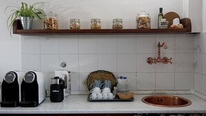 A kitchen with a white tiled backsplash, a copper sink, a coffee maker, a kettle, a plant in a metal pot, and jars of nuts on a shelf. - Bed & Breakfast La Pecora Nera (Belluno)
