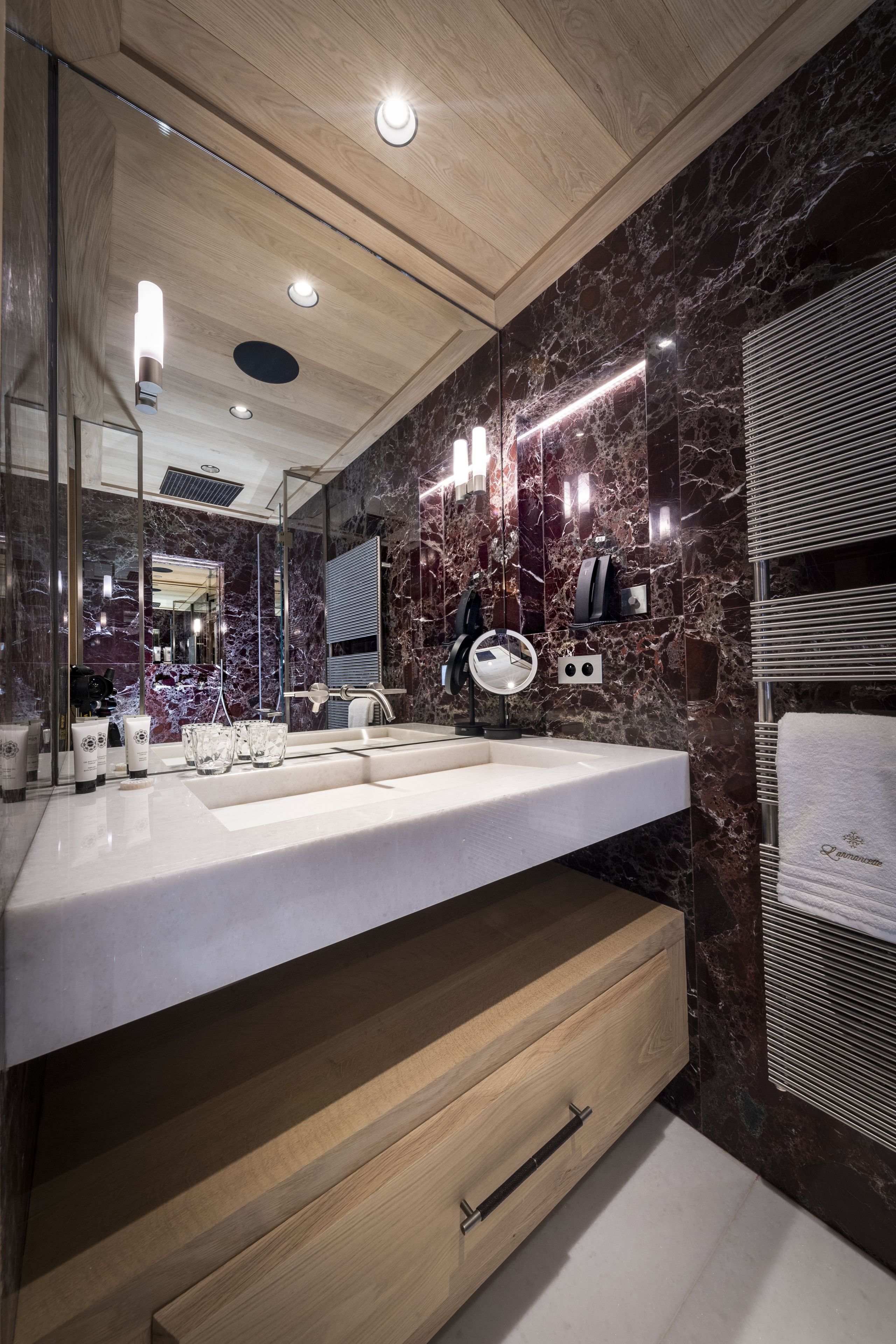 A modern bathroom with a marble backsplash, a wooden vanity, a large mirror, and built-in lighting.