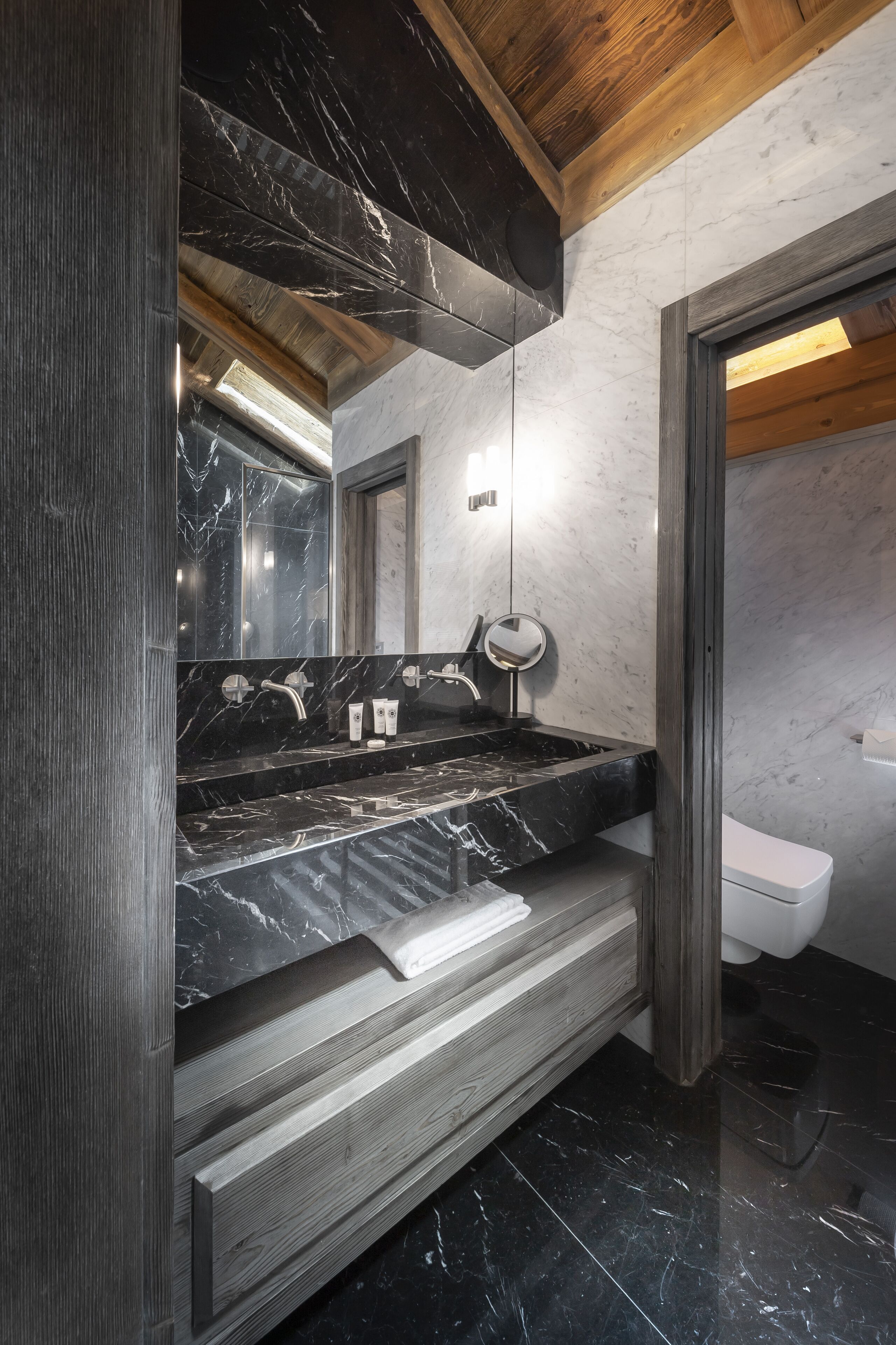 Un baño moderno con tocador de mármol negro, techo de madera y un inodoro blanco.