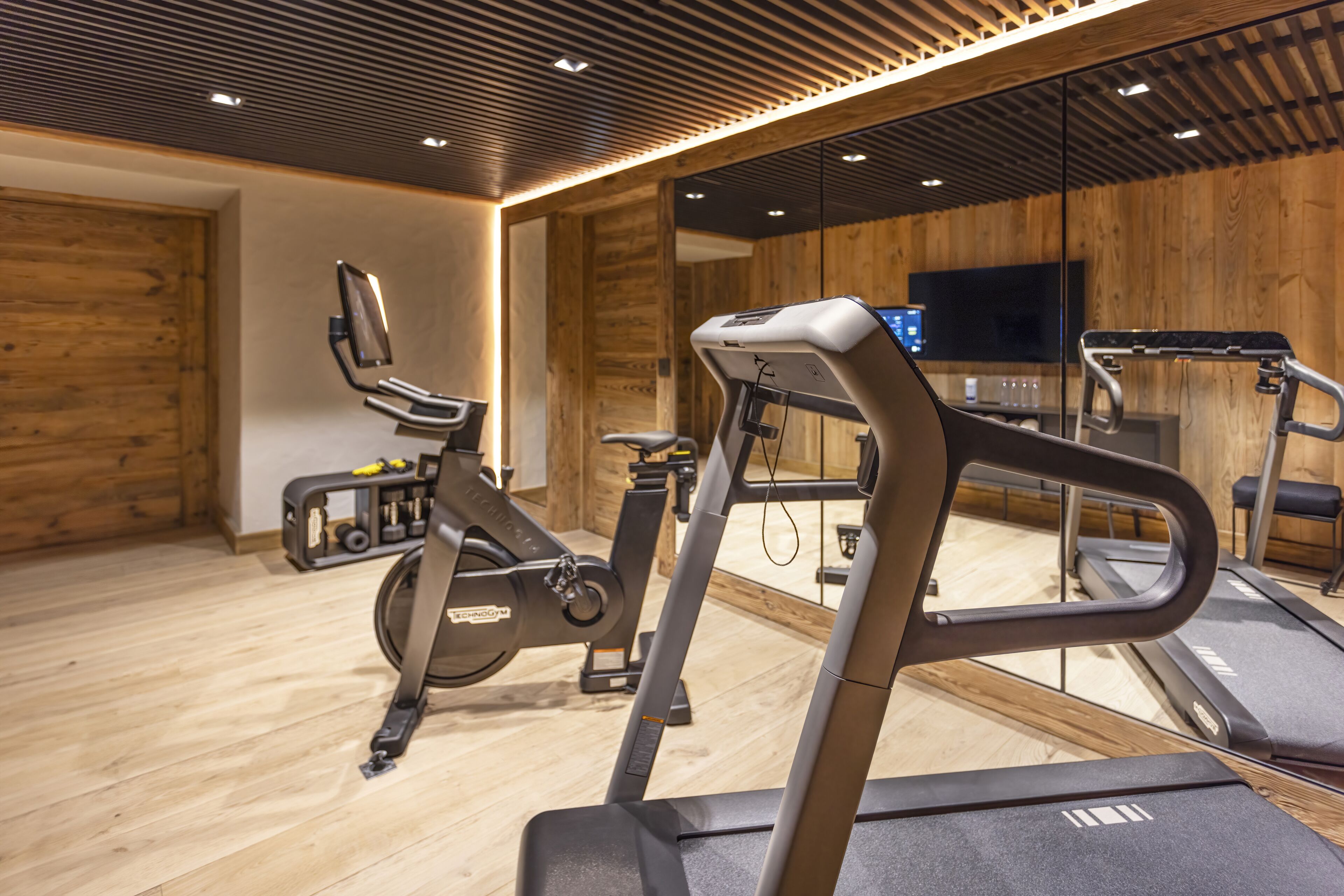 A gym with exercise equipment, a mirrored wall, and a television.