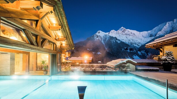 Una piscina con montagne sullo sfondo, architettura in legno e paesaggio innevato.
