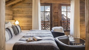 Accogliente camera in legno con un letto, una sedia, un tavolino e una finestra vista montagna.