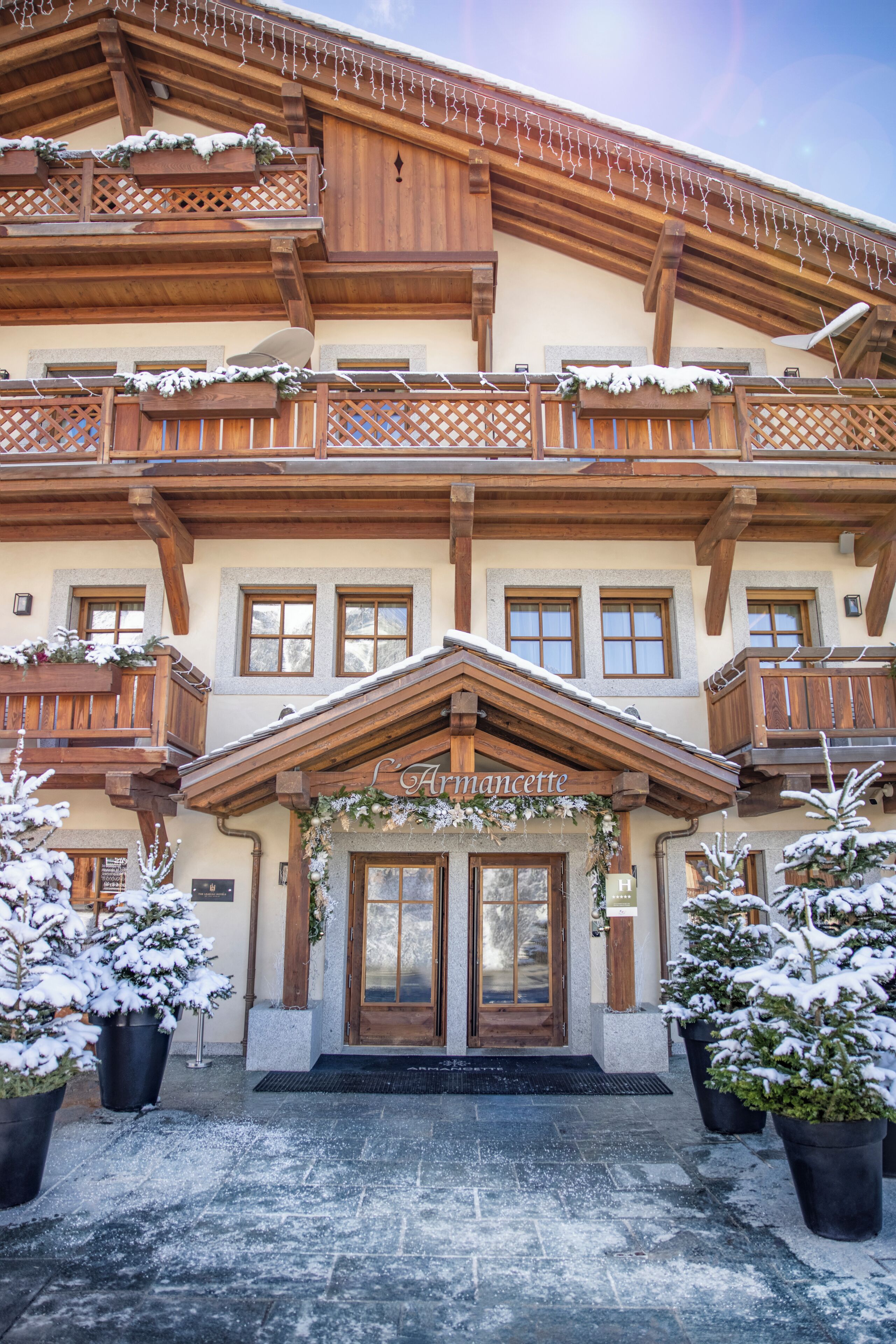 Un edificio de estilo chalete tradicional con balcones de madera, un letrero que dice "L'Armancette" y plantas nevadas en la parte delantera.