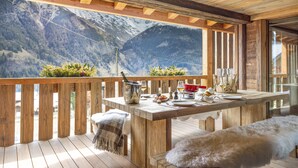 Un'area esterna con terrazza in legno e tavolo apparecchiato per mangiare, con vista su un paesaggio montuoso.