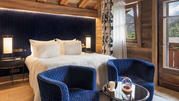 Ein gemütliches Zimmer mit einem großen Bett, zwei blauen Sessel, einem kleinen Tisch mit Tasse und Glas sowie einem Fenster mit Vorhängen.