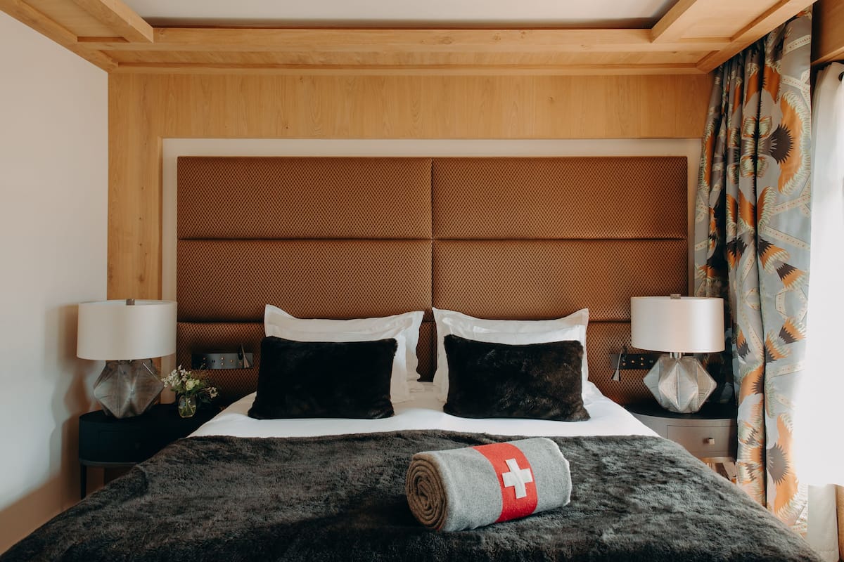 Habitación de hotel con una cama grande, dos lámparas de noche, un cabecero de madera y una cortina decorativa.