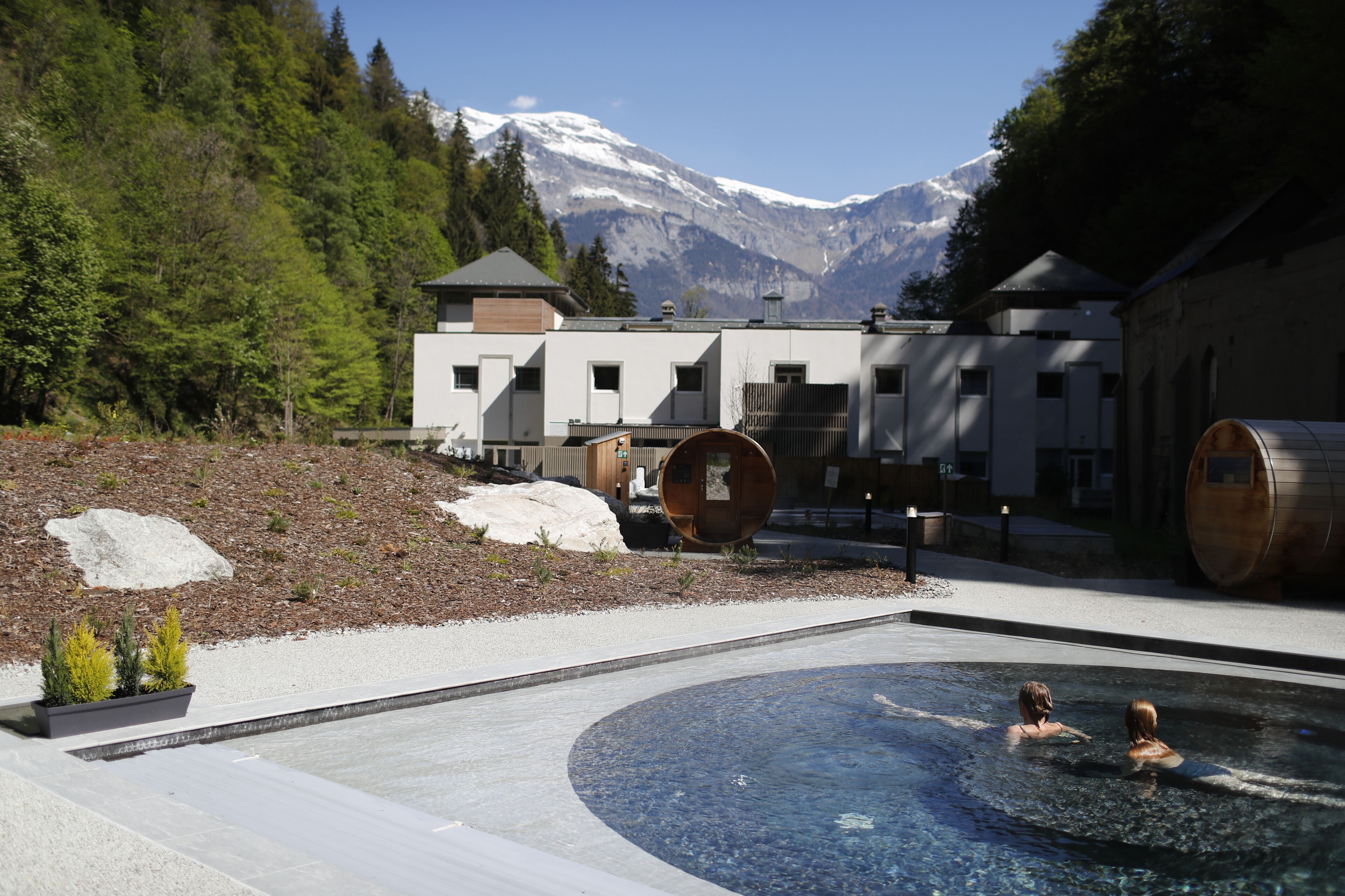 Un spa modern amb una piscina, envoltat d'un paisatge muntanyós i tones de fusta.