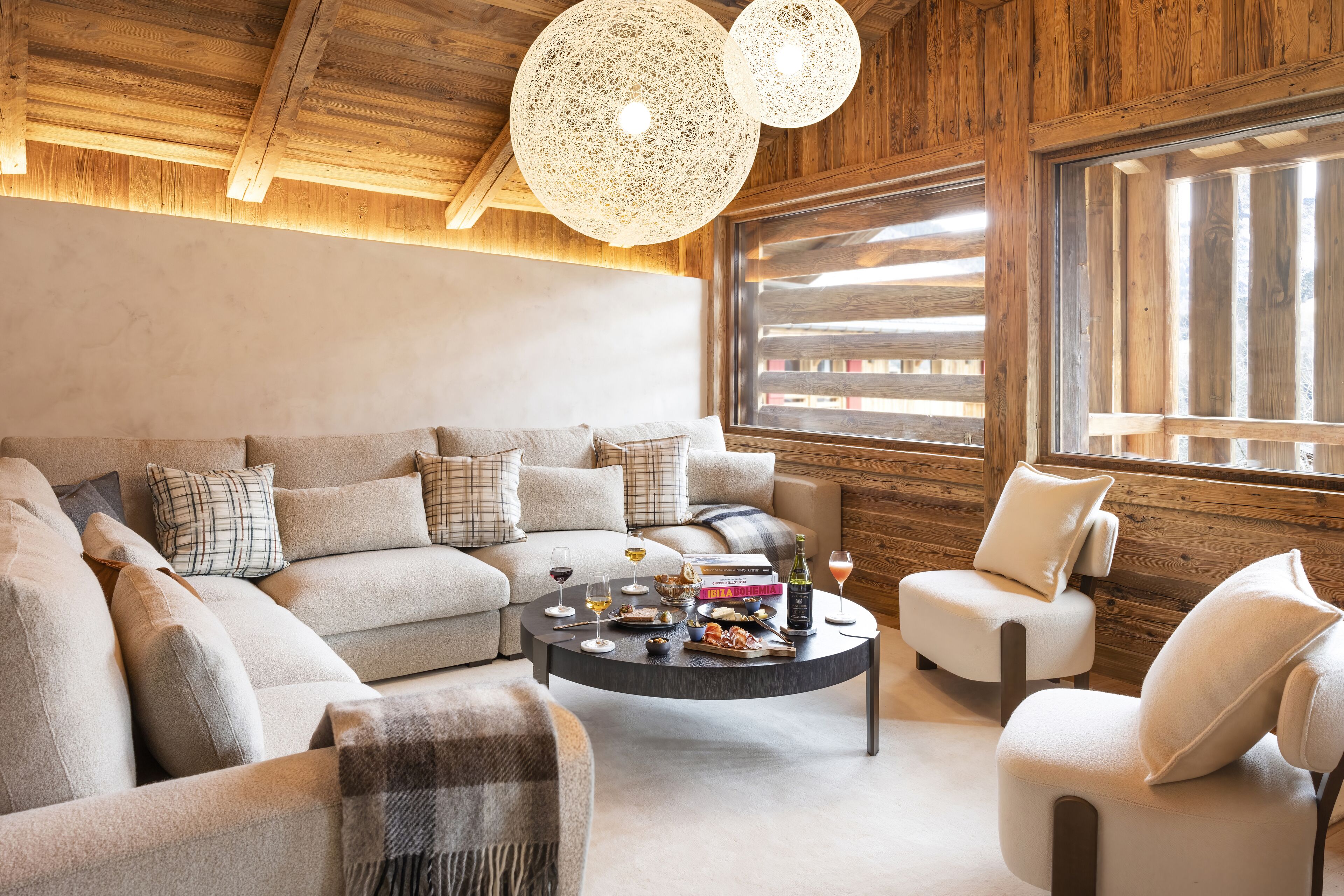 Un salon chaleureux avec un canapé d’angle, une table basse et une fenêtre équipée de stores en bois.