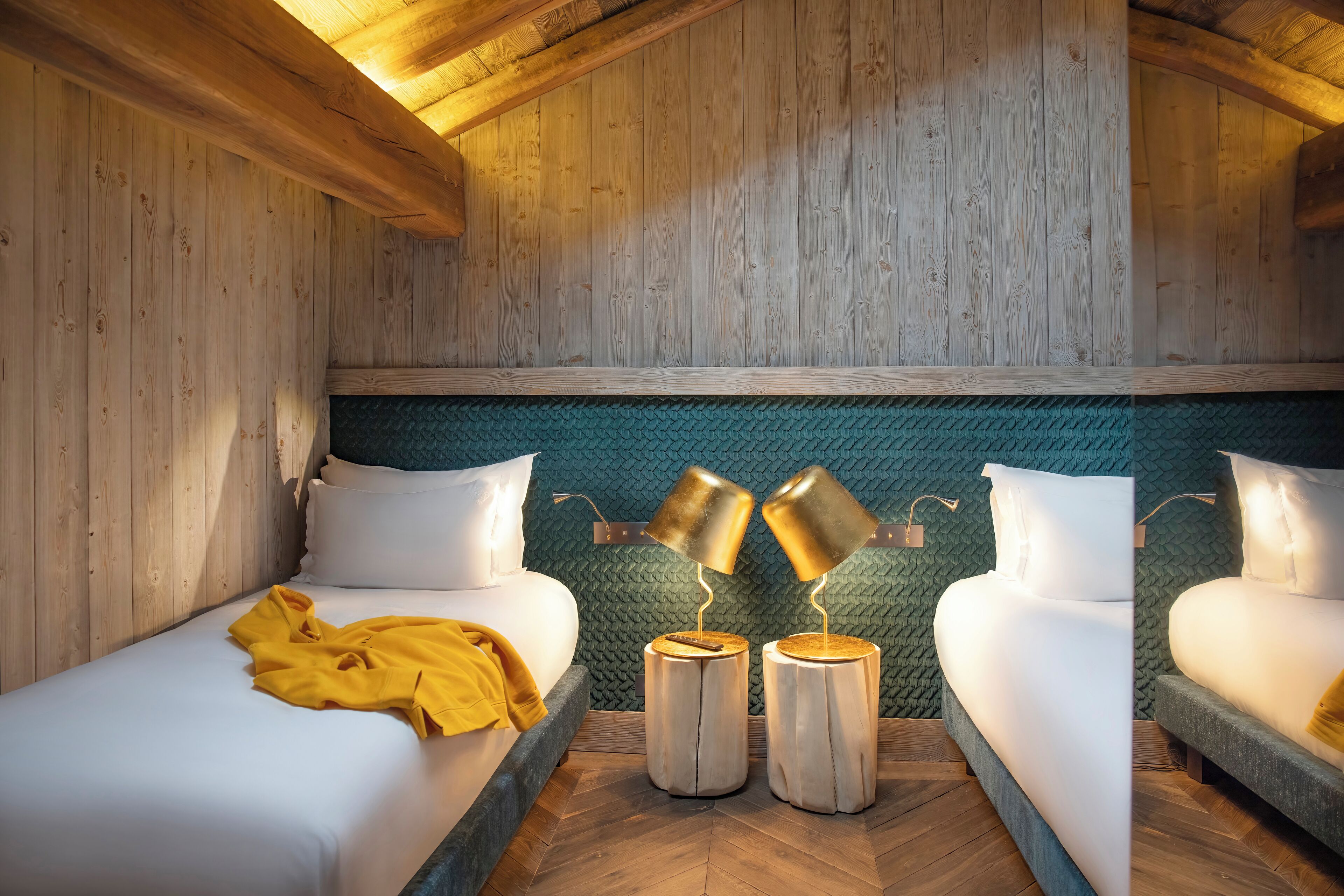A cozy room with wooden walls, a green textured wall behind the bed, and two bedside tables with lamps.